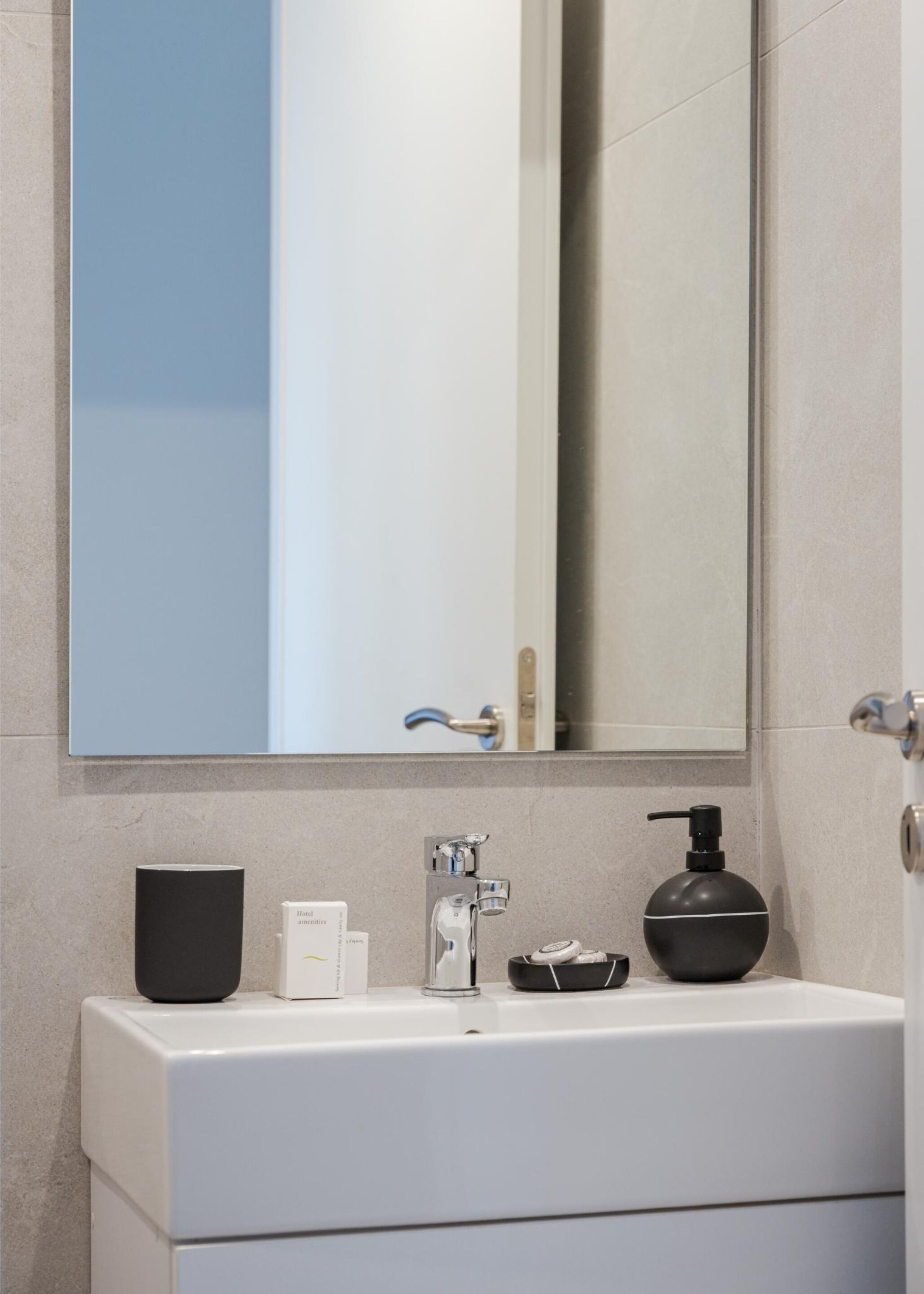 A modern bathroom with a white sink, a black soap dispenser, and a mirror above it.