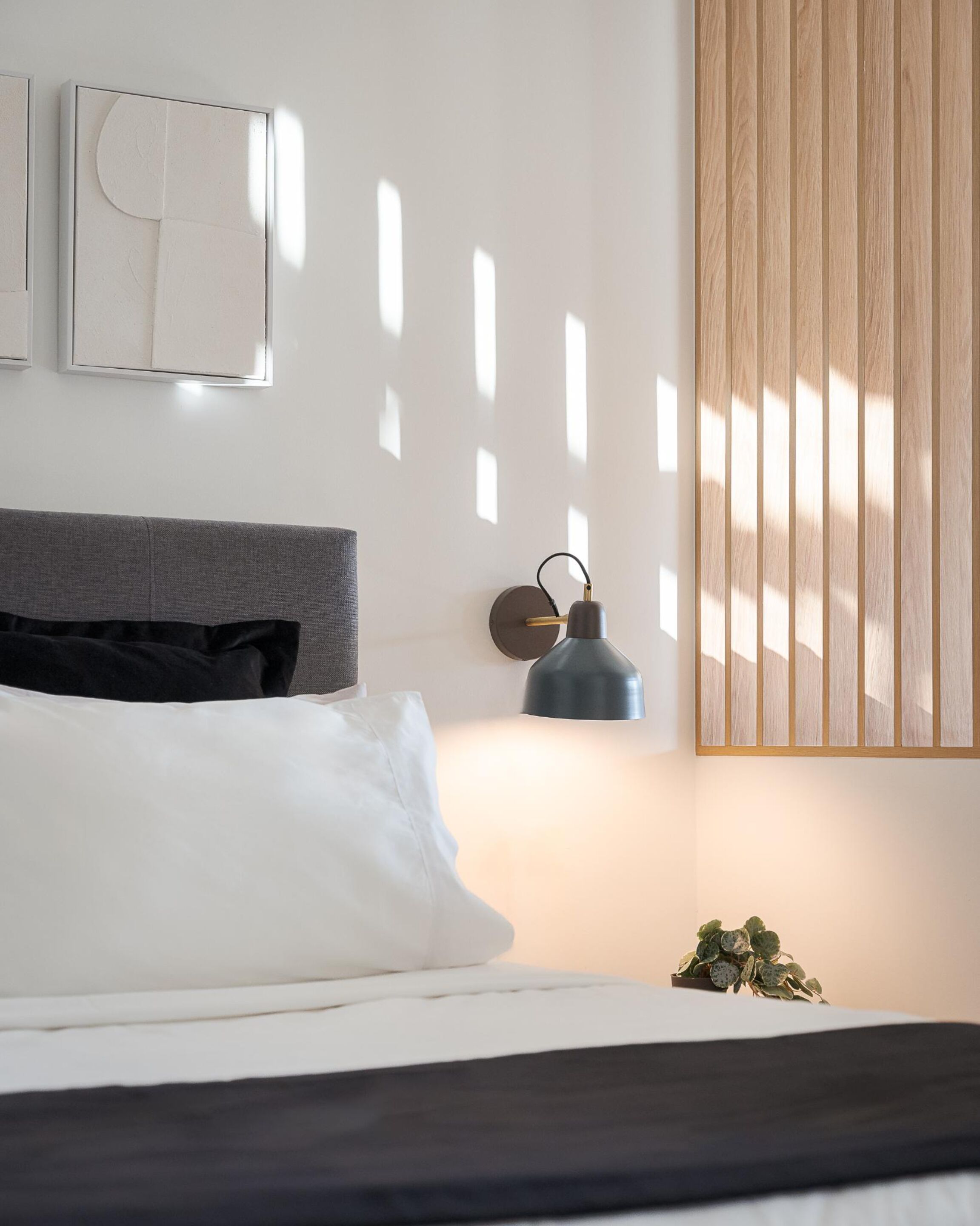 A neatly made bed with white and black bedding, a grey headboard, and a wall-mounted lamp.