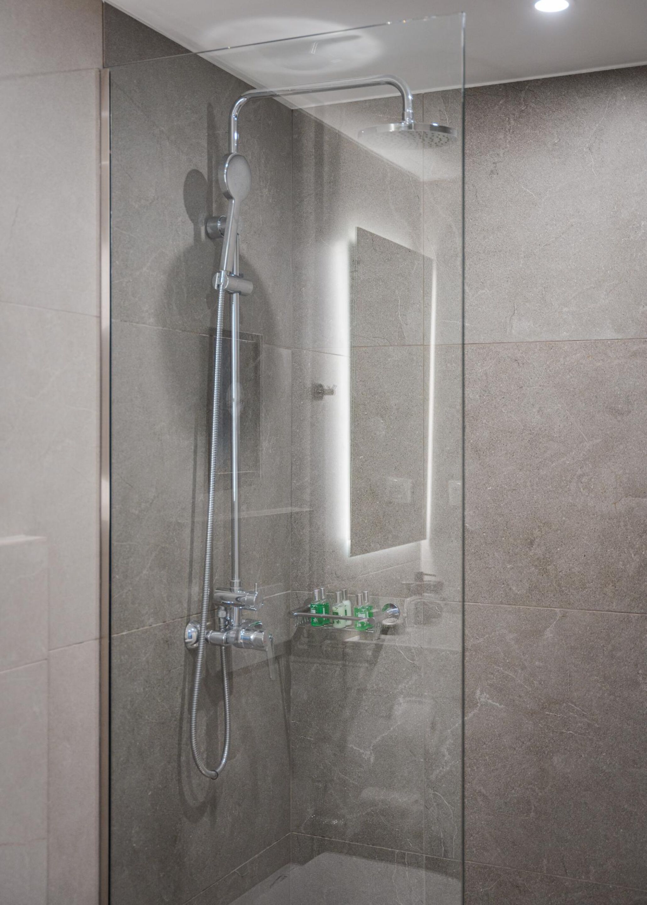 A glass-enclosed shower with a handheld showerhead and a wall-mounted faucet.