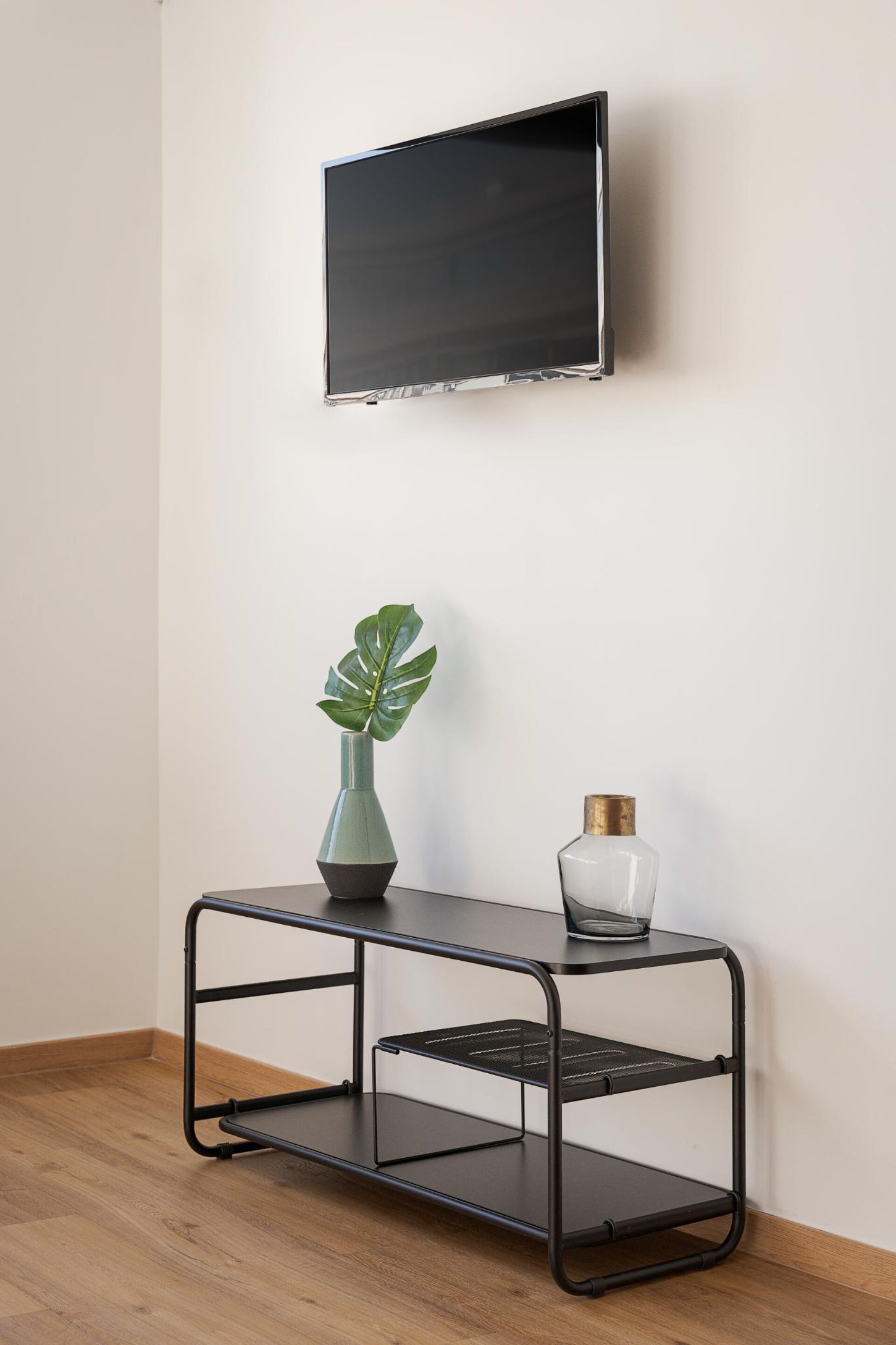 A black metal TV stand with a vase and a glass bottle against a white wall.