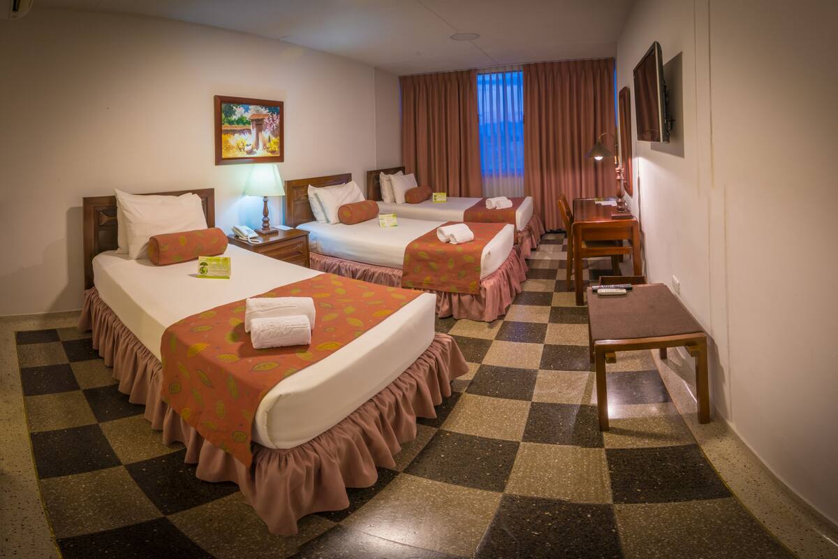 A hotel room with two beds, a desk, a chair, a lamp, and a painting on the wall.