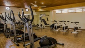 A gym with various cardio and strength training equipment, wooden floors, and a ceiling fan. - Hotel Chicala S.A.S (Neiva)