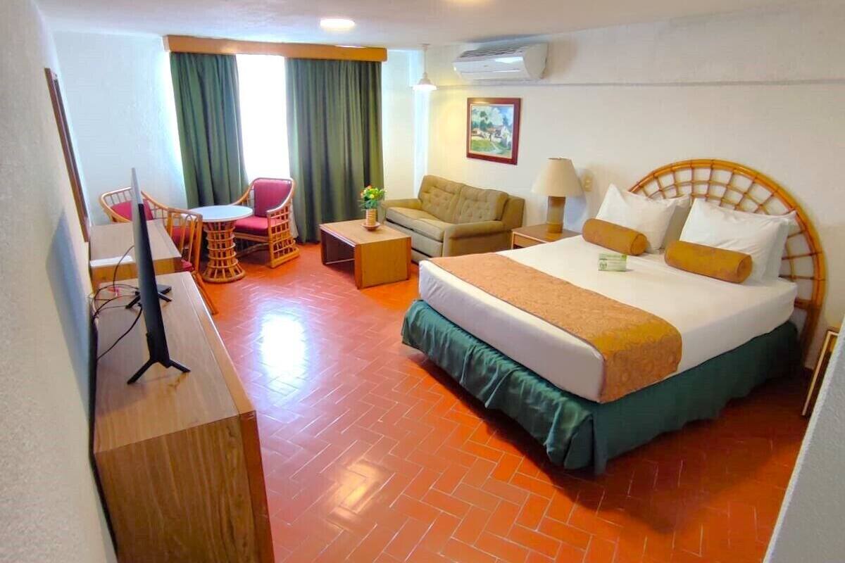A hotel room with a bed, a desk, a chair, and a sofa.