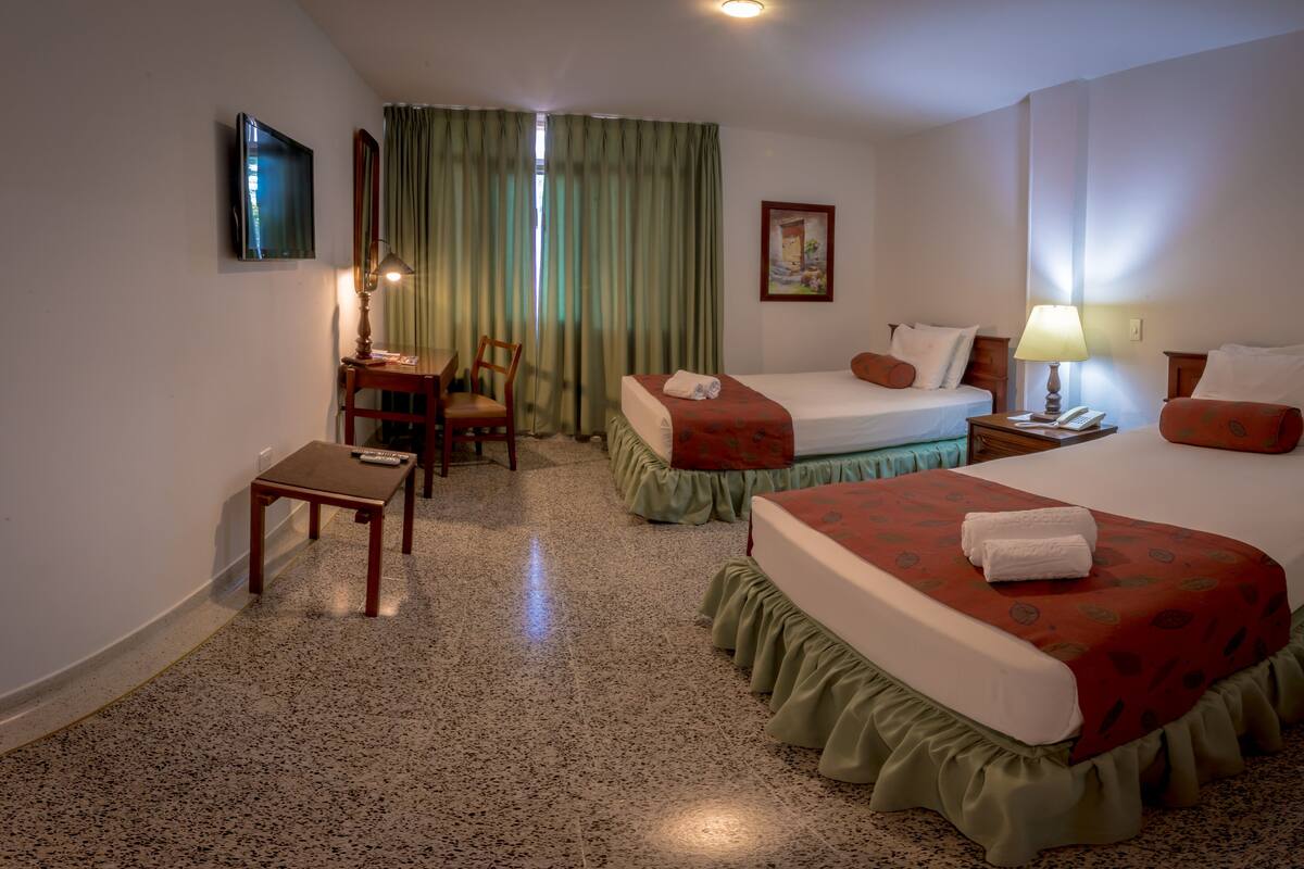 A hotel room with two beds, a desk, a chair, a TV, and a painting on the wall.