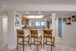 A kitchen with a central island, three wooden bar stools, and a view to the outside.