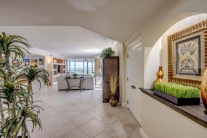 A spacious living area with a dining table, potted plants, and a decorative wall piece.