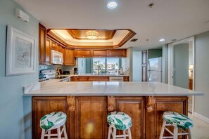 A modern kitchen with wooden cabinets, a large island with bar stools, and a view to the outside.