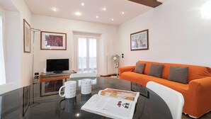 A modern living room with a glass table, a flat-screen TV, an orange sofa, and framed artwork on the walls. - Italianway Easy - Tadino 13 B (Milan)