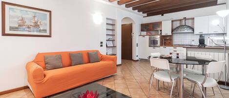 A modern living room with a sofa, a glass coffee table, and a dining area with a table and chairs.