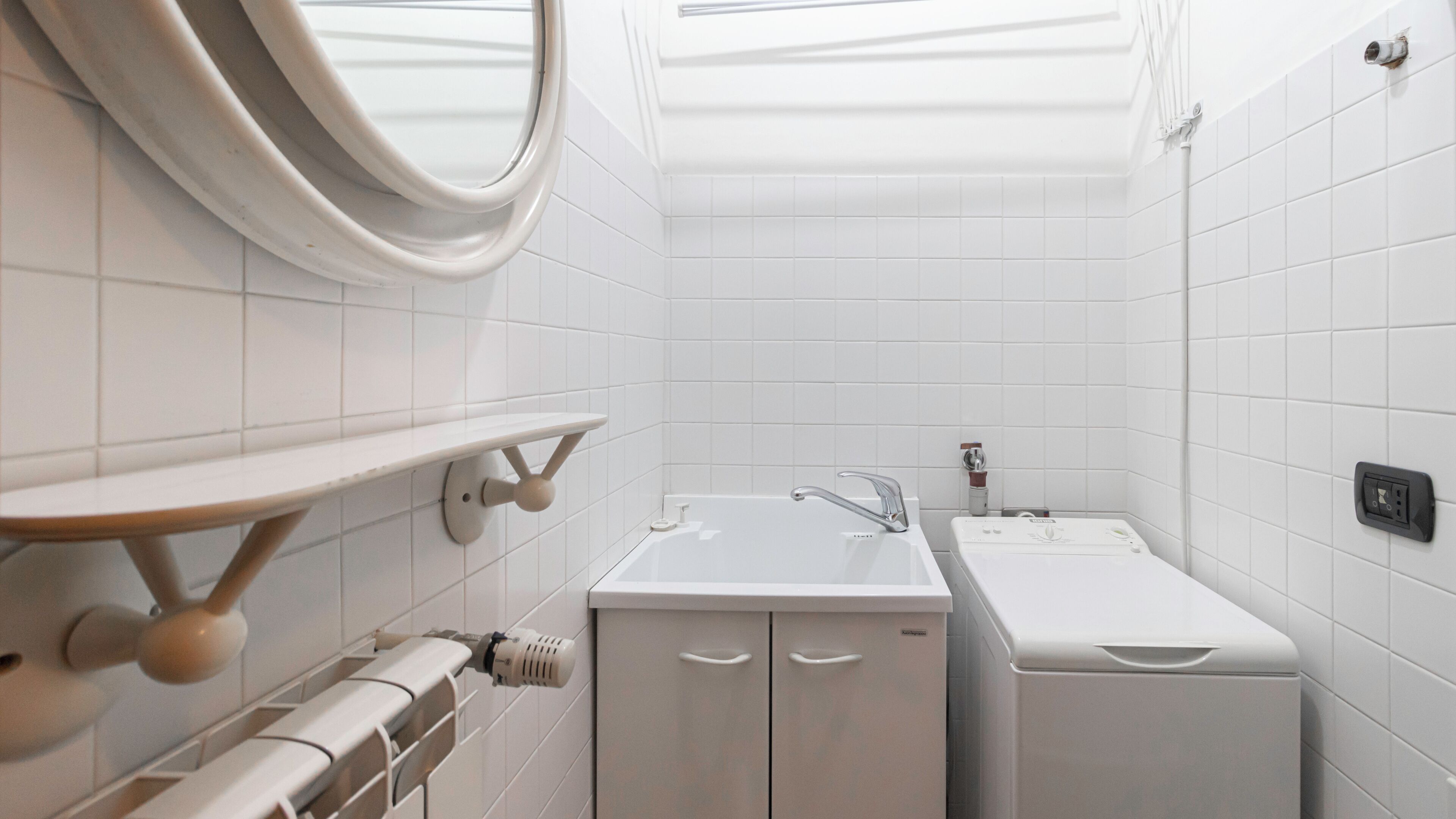 A small, modern bathroom with white tiles, a sink, a mirror, and a towel rack.