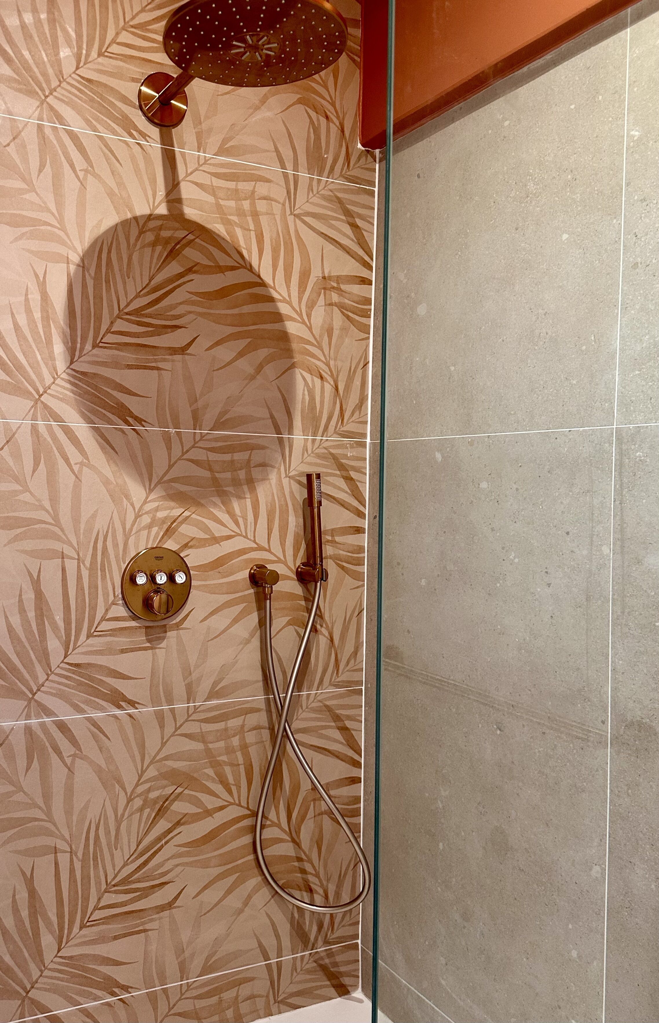 A shower with a leaf-patterned wall, a glass partition, and a control panel with three buttons.