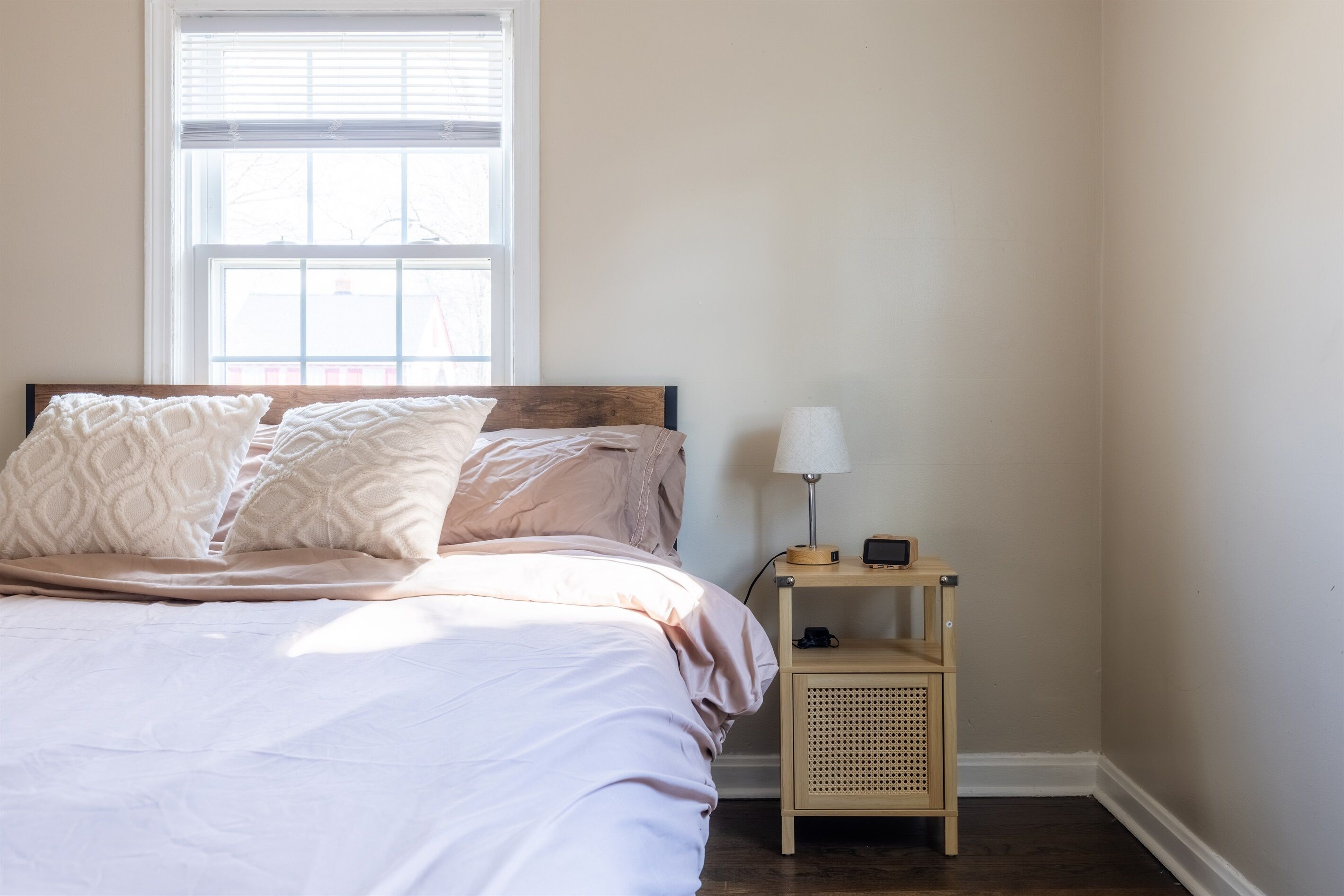 A bedroom with a bed, a nightstand, a lamp, and a window.