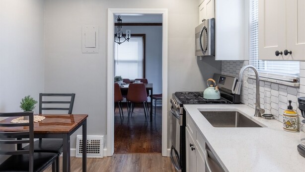 Une cuisine moderne avec un coin repas, un plancher en bois et des meubles de rangement blancs.