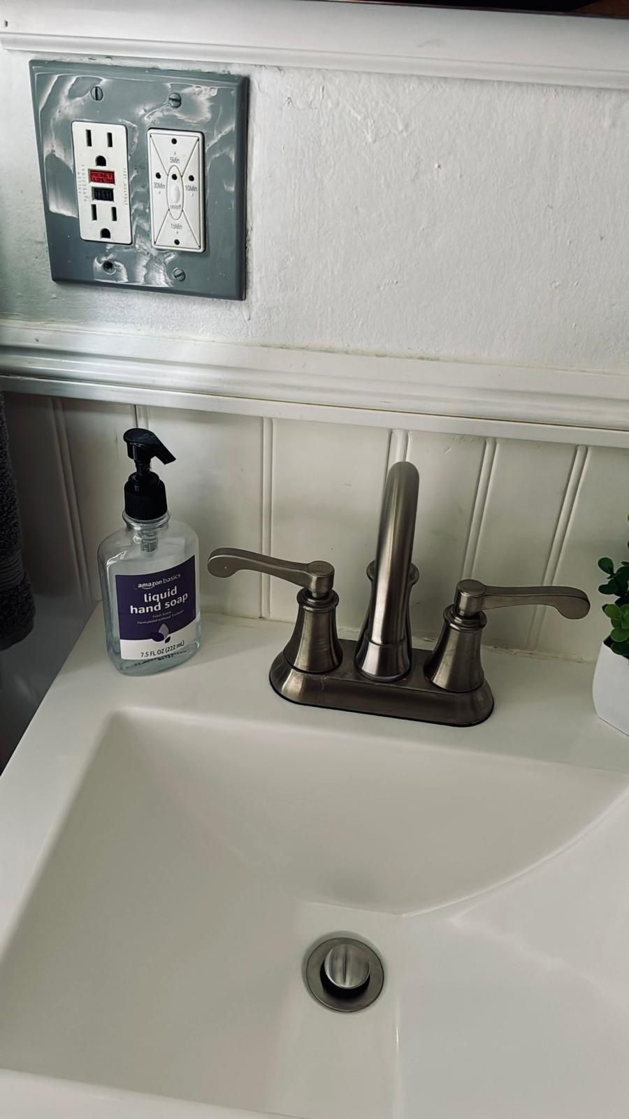 A bathroom sink with a modern faucet, a hand soap dispenser, and a power outlet above the sink.