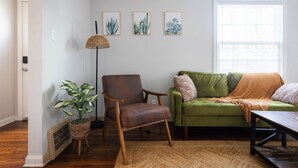 Un salon avec un canapé vert, un fauteuil en cuir marron, une lampe sur pied et une plante en pot.