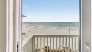 A beach view from a balcony with a white railing, a clear sky, and a flag on the sand. - Beach House - Whale Rested by PHG (Panama City Beach)