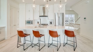 A modern kitchen with white cabinetry, a large island with bar stools, stainless steel appliances, and pendant lighting. - Beach House - Whale Rested by PHG (Panama City Beach)