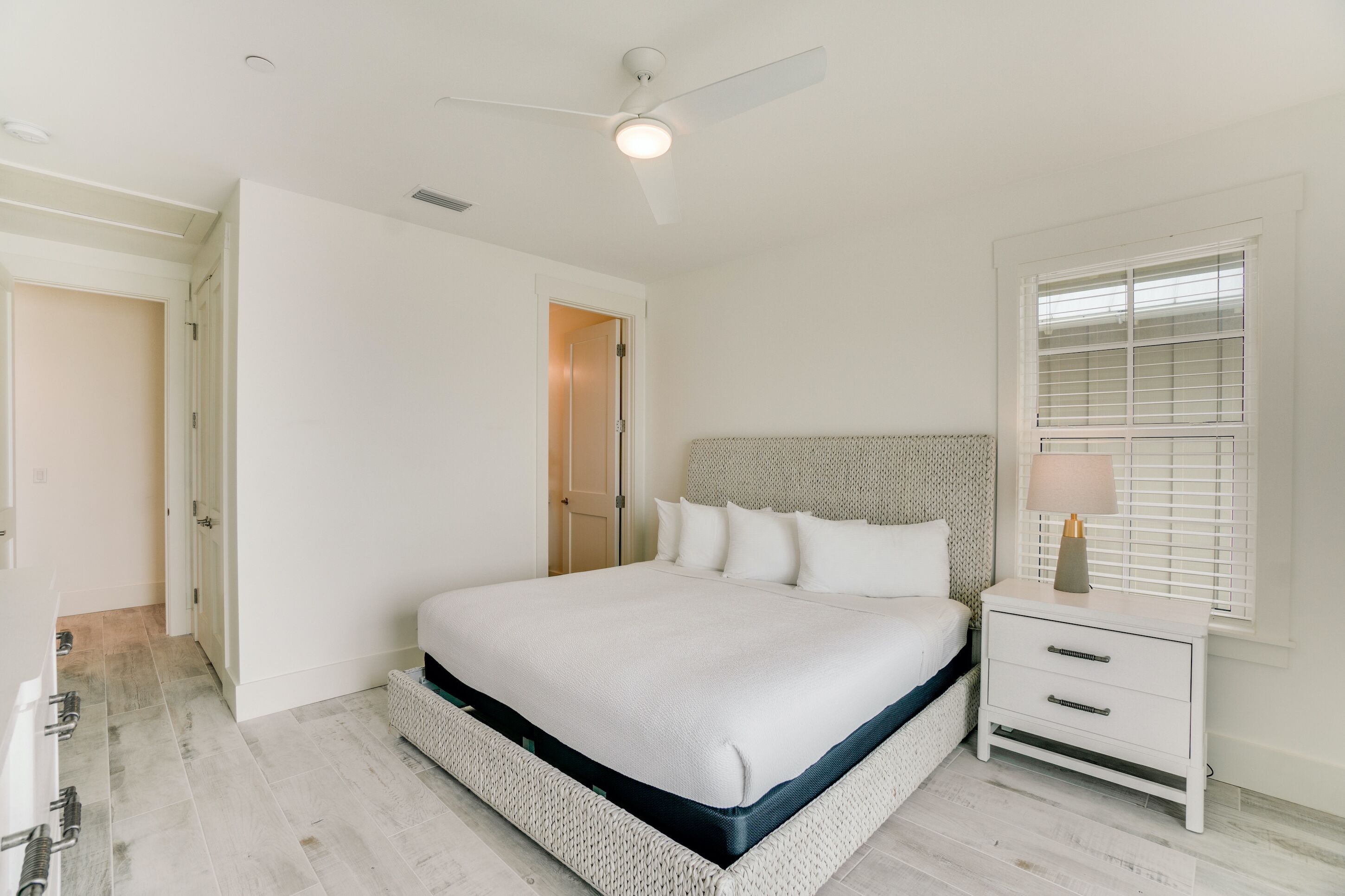 A bedroom with a bed, a nightstand, a lamp, a ceiling fan, and a window with blinds.