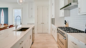 A modern kitchen with white cabinetry, a large island with a sink, a gas stove, and pendant lighting. - Beach House - Whale Rested by PHG (Panama City Beach)