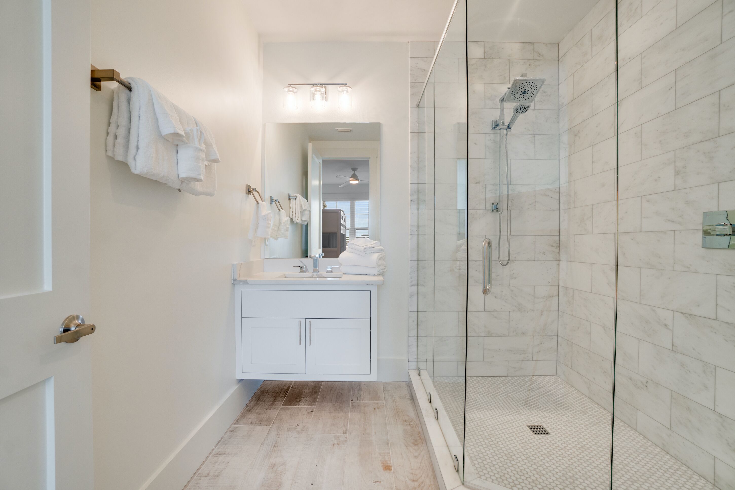 A modern bathroom with a glass-enclosed shower, white cabinetry, and a visible ceiling fan.
