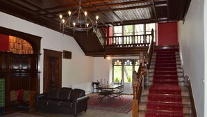 A spacious living room with a fireplace, leather sofa, and a dining table. A wooden staircase with a red carpet leads to an upper level.