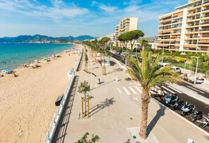A beachside promenade with a row of palm trees, a pedestrian walkway, and a parked motorcycle.