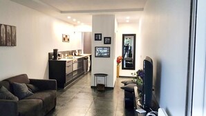 A modern living room with a sofa, a television, and a kitchen area with cabinets and a coffee machine. - Renovated Apartment With Terrace Facing THE SEA (Cannes)