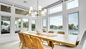 A spacious dining area with a large wooden table, wicker chairs, and a modern chandelier. - New House, Waterfront, Pool, Hot Tub, Golf Cart (Indian Rocks Beach)