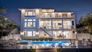 A multi-story house with a swimming pool, outdoor seating, and a staircase leading to the upper floor. - New House, Waterfront, Pool, Hot Tub, Golf Cart (Indian Rocks Beach)