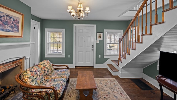 A living room with a sofa, a wooden coffee table, a chandelier, a staircase, and a fireplace. - Historic District: Downtown New Bern (New Bern)