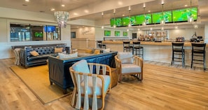 A bar area with multiple screens, a sofa, and wicker chairs.