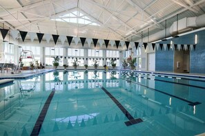 Ein Hallenbad mit klarem Wasser, hoher Decke und Blumentöpfen entlang der Wände.