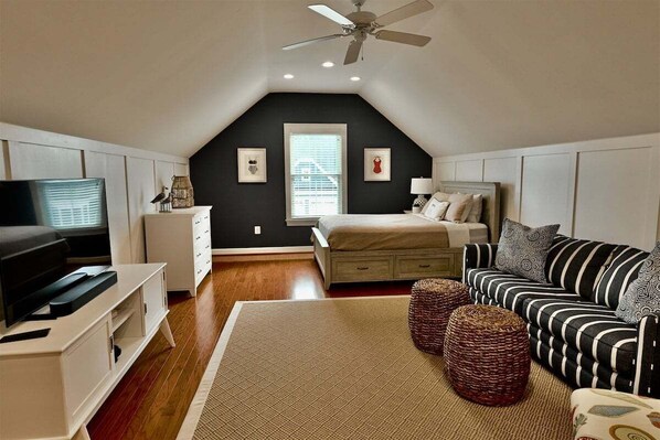 A bedroom with a bed, a TV, a ceiling fan, and a window.