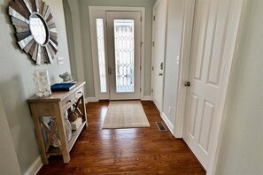 Un couloir doté d’un plancher en bois, d’un miroir décoratif, d’une console avec espace de rangement et d’une porte avec un panneau en verre.