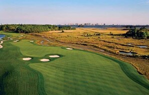 Un parcours de golf avec des bunkers de sable, des obstacles d’eau et, en arrière-plan, la silhouette de la ville.