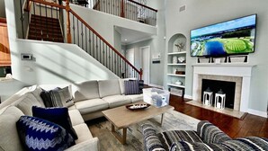 A living room with a sofa, a coffee table, a fireplace, a TV, and a staircase. - Bayside Resort 5BR, 4 Full Baths 2 Suite Luxury Ho (Selbyville)