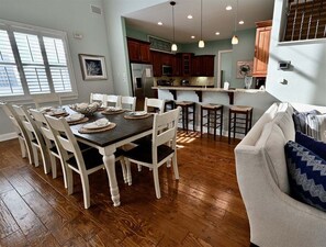 A dining area with a wooden table and chairs, a kitchen with dark wooden cabinets, and a light-colored sofa.