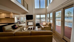 A spacious living area with a large window overlooking a body of water, a flat-screen TV, and a comfortable seating arrangement. - Bethany Beach Waterfront House w Stunning Views * (Bethany Beach)