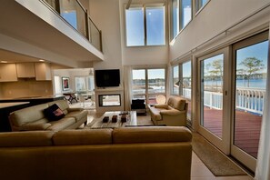 A spacious living area with a large window overlooking a body of water, a flat-screen TV, and a comfortable seating arrangement.