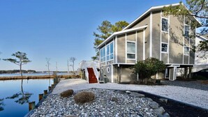 A two-story house with a red staircase, a dock extending into a body of water, and a clear sky. - Bethany Beach Waterfront House w Stunning Views * (Bethany Beach)