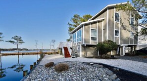 A two-story house with a red staircase, a dock extending into a body of water, and a clear sky.
