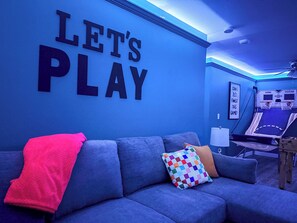 Una habitación con pared azul, un sofá, un cojín colorido y un aro de baloncesto.