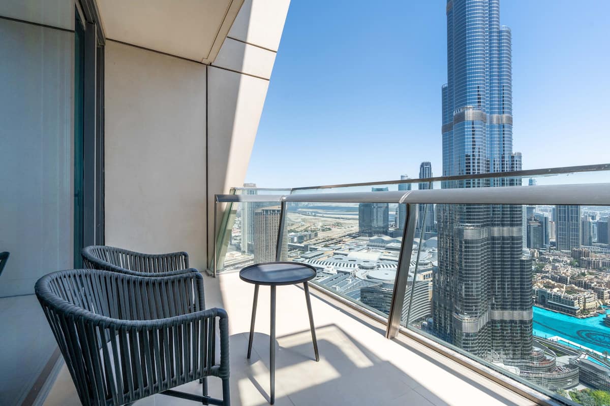 A balcony with two wicker chairs and a small table, overlooking a cityscape with a prominent skyscraper.