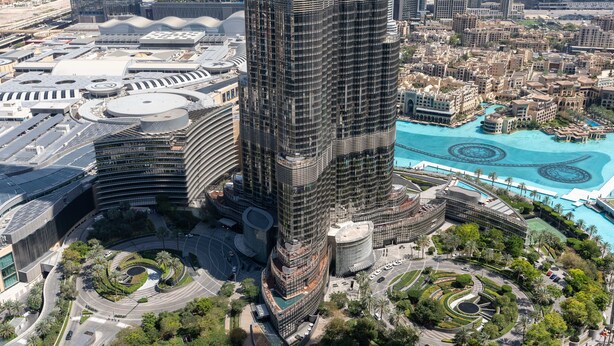 A high-rise building with a unique circular design, surrounded by a landscaped area with palm trees and a pool.