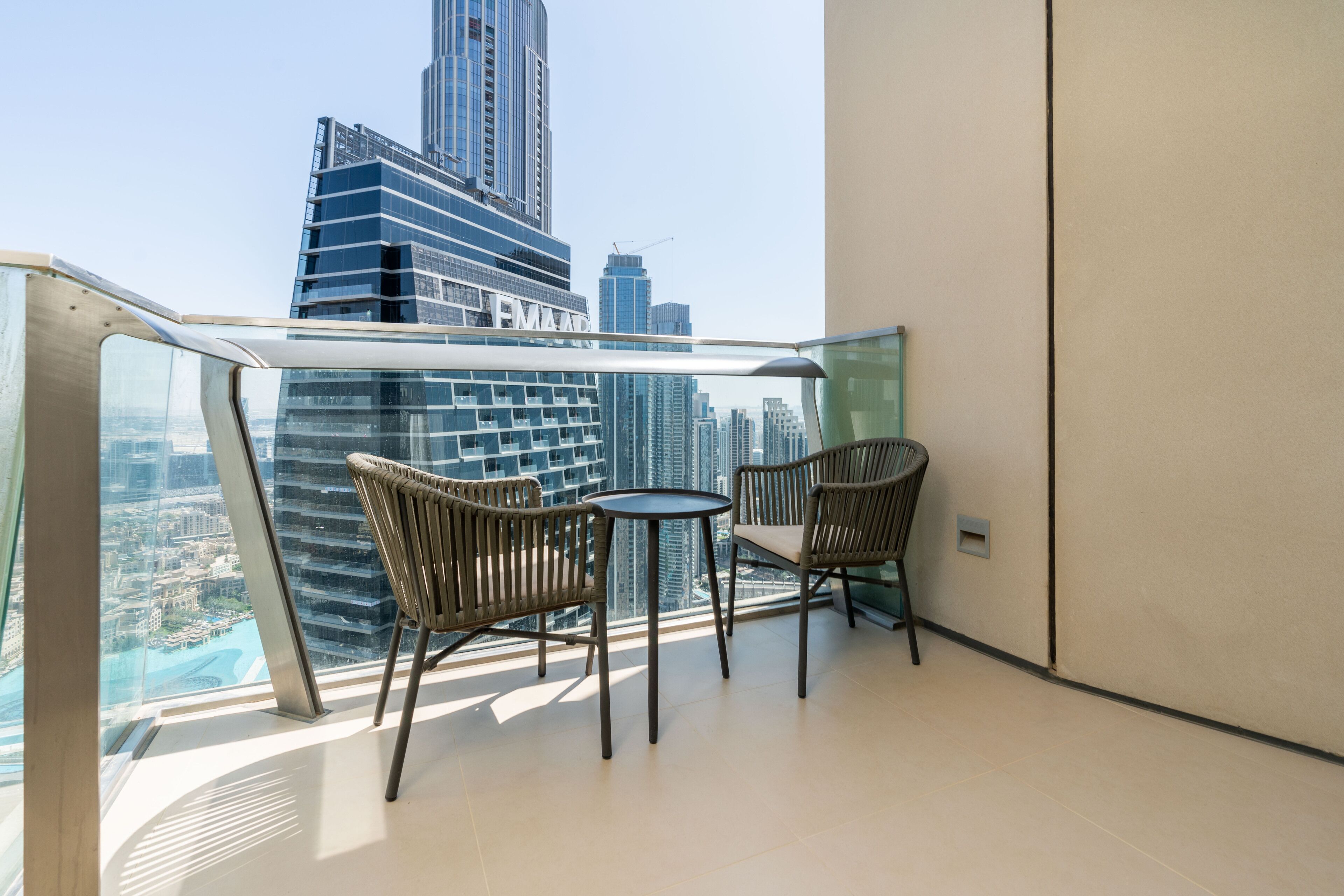 A balcony with two wicker chairs and a small round table, overlooking a cityscape with high-rise buildings.