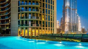 A hotel with a swimming pool, a modern building with a curved facade, and a tall skyscraper in the background.