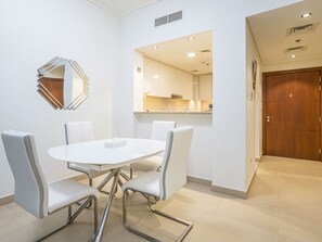 A modern dining area with a white table and chairs, a decorative mirror, and a view into a kitchen. - Vacay Lettings - Burj Vista Tower 1 (Dubai)