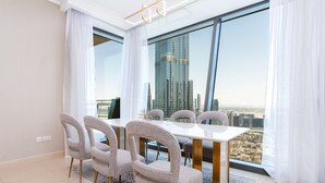 A dining area with a white table and chairs, large windows with a city view, and a modern chandelier.
