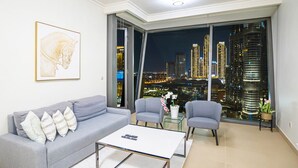 A modern living room with a grey sofa, two armchairs, a coffee table, and a large window offering a city view at night.