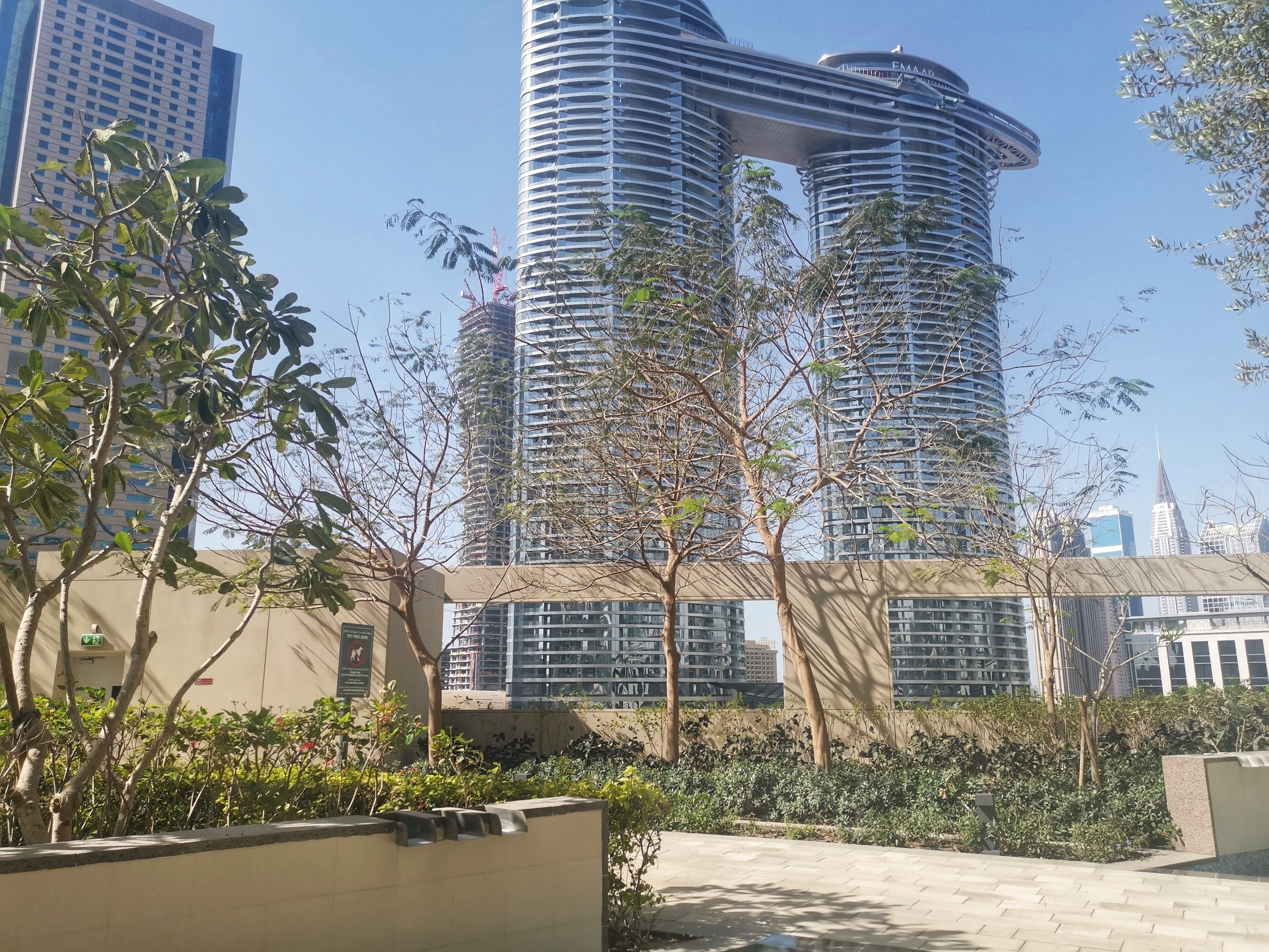 A modern high-rise building with a unique curved design, surrounded by greenery and other high-rise buildings in the background.